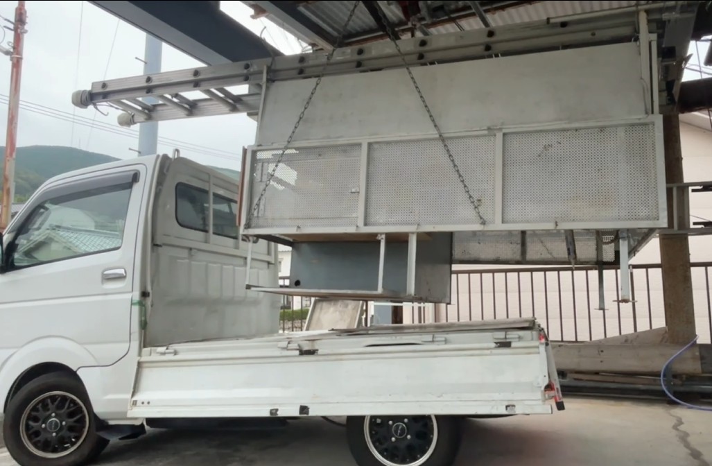単管パイプで組んだホイストから、軽トラの荷台がチェーンで吊り上げられ、車体から完全に浮いている状態